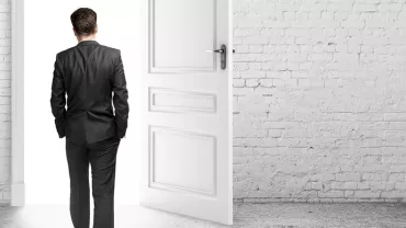 Man in a suit walking through an open door in a white brick room